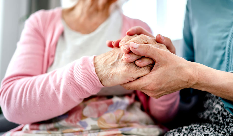 Close-up of a caregiver holding an elderly patient's wrinkled hand in comfort, representing the ongoing, supportive hospice care provided by Homage Hospice Plus in the Dallas-Fort Worth area.